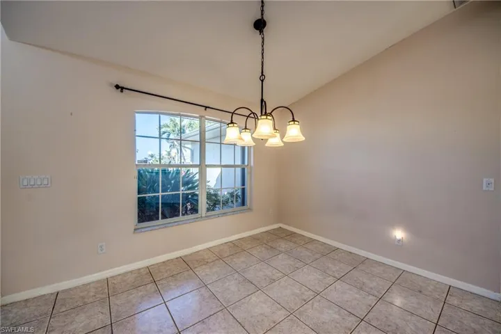 Unfurnished room featuring an inviting chandelier, lofted ceiling, and light tile patterned floors