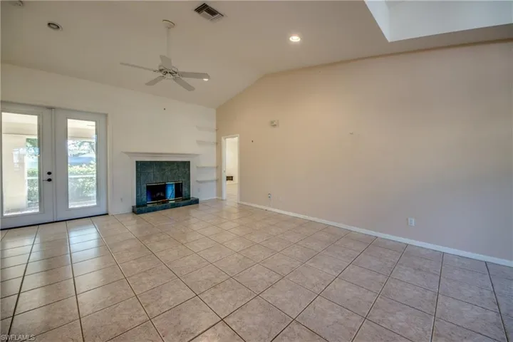 Unfurnished living room featuring light tile patterned flooring, french doors, vaulted ceiling, ceiling fan, and a premium fireplace