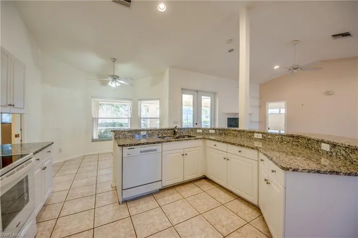 Kitchen with sink, vaulted ceiling, stone counters, white appliances, and white cabinets