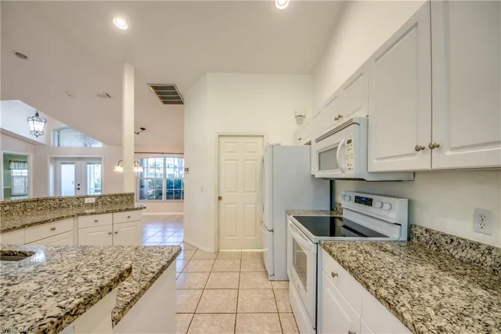 Kitchen with lofted ceiling, white cabinetry, light tile patterned floors, white appliances, and light stone countertops