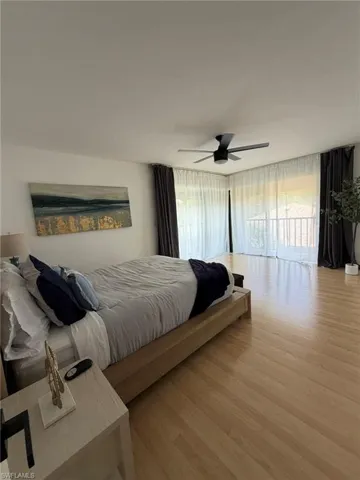 Bedroom featuring light wood-finish flooring, a contemporary ceiling fan, and expansive glass doors opening to a balcony with white railings