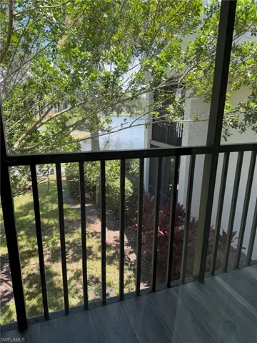 Screened balcony with wood-finish flooring, offering a partial water body view and surrounding trees