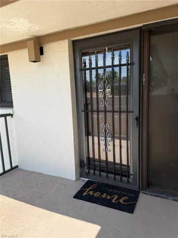 Entryway featuring a decorative wrought iron security door, textured stucco exterior, and a contemporary wall-mounted light fixture