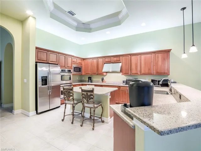 Kitchen featuring stainless steel appliances, light stone counters, a kitchen bar, and decorative light fixtures