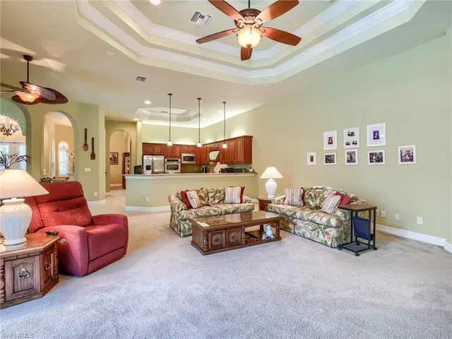 Carpeted living room with ceiling fan, a raised ceiling, and crown molding