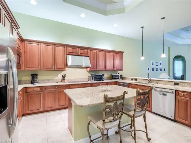 Kitchen with hanging light fixtures, a raised ceiling, a breakfast bar area, stainless steel appliances, and sink