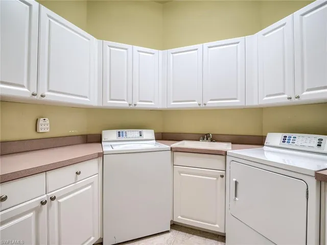 Clothes washing area with light tile patterned flooring, sink, washer and dryer, and cabinets