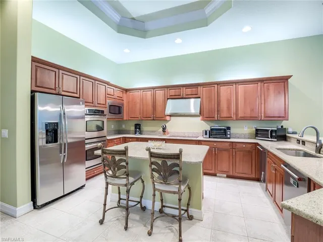 Kitchen featuring light stone counters, sink, a tray ceiling, appliances with stainless steel finishes, and a breakfast bar