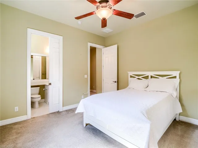 Carpeted bedroom featuring ceiling fan and ensuite bath