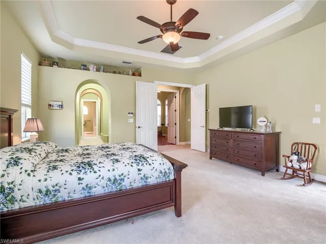Carpeted bedroom featuring ornamental molding, ensuite bath, ceiling fan, and a raised ceiling