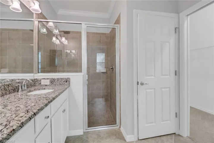 Bathroom with crown molding, a shower stall, baseboards, tile patterned floors, and vanity