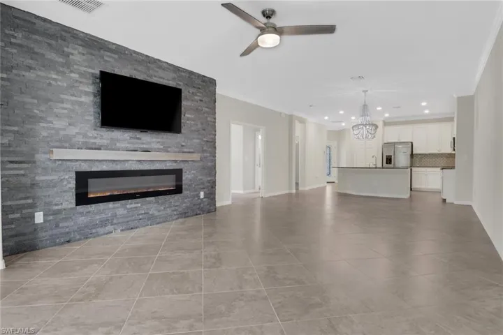 Unfurnished living room featuring ceiling fan with notable chandelier, tile patterned flooring, crown molding, and a fireplace