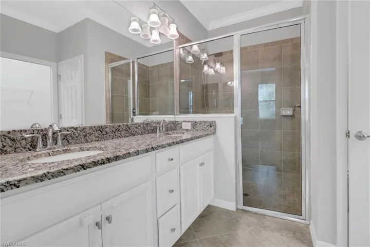 Full bath with ornamental molding, a sink, an inviting chandelier, and a shower stall
