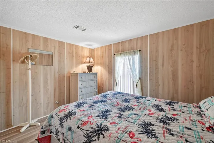 This room features wood paneling, a textured white ceiling, and a window with blinds and sheer curtains
