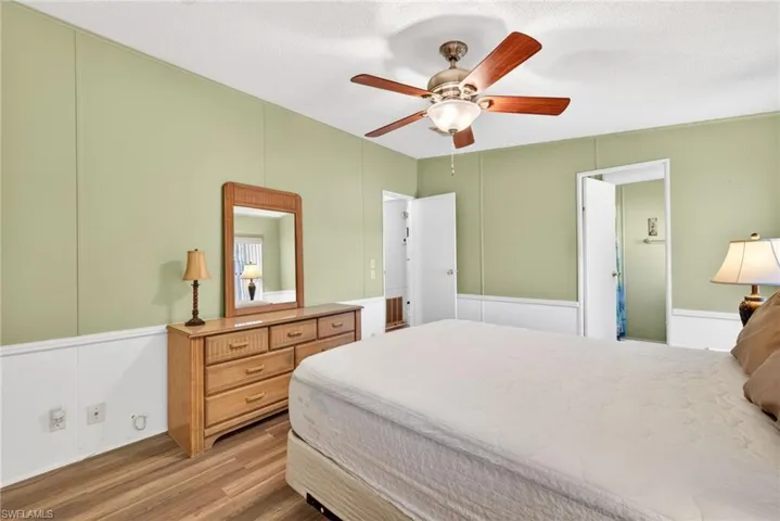 Bedroom featuring a light green wall and white wainscoting, wood-look flooring, and a ceiling fan with light fixture