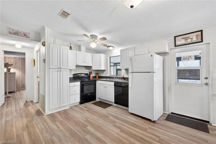 The kitchen features white cabinetry, dark countertops, and a full suite of appliances, including a white refrigerator, black range, and black dishwasher
