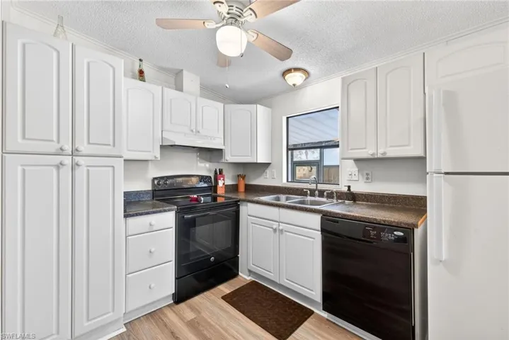 The kitchen features white cabinetry, a double basin sink, and a combination of black and white appliances