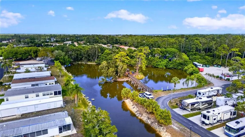 Aerial view showcasing the community's serene lake with a wooden footbridge and lush surrounding greenery