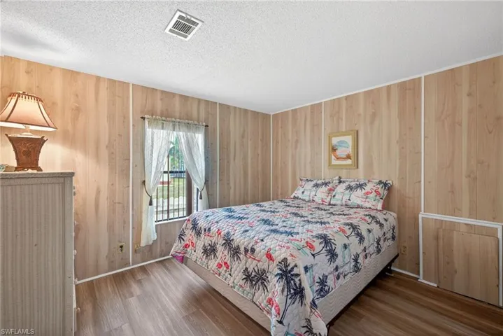 Bedroom featuring light wood paneling, wood-style flooring, and a window with white curtains