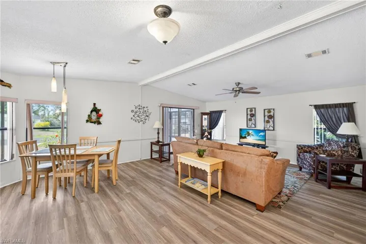 The open-concept living area features wood-look flooring, ample natural light from several windows, and a ceiling fan