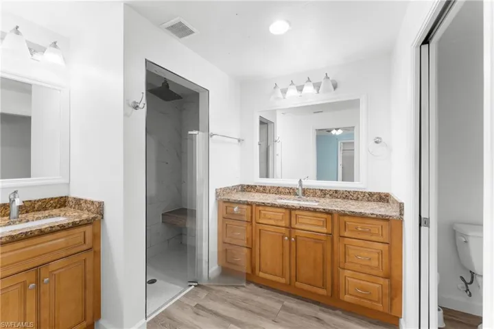 Bathroom featuring two vanities, a marble finish shower, and light wood finished floors