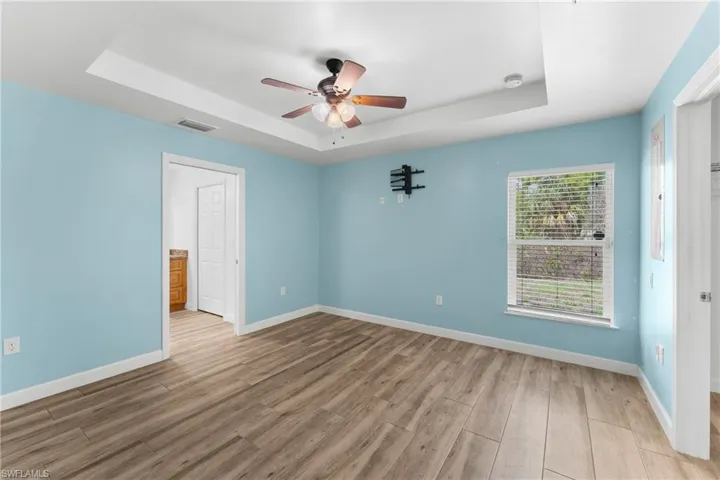 Unfurnished bedroom with a raised ceiling, light wood finished floors, and ceiling fan