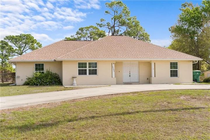 Ranch-style house featuring stucco siding, a front lawn, a shingled roof, and curved driveway