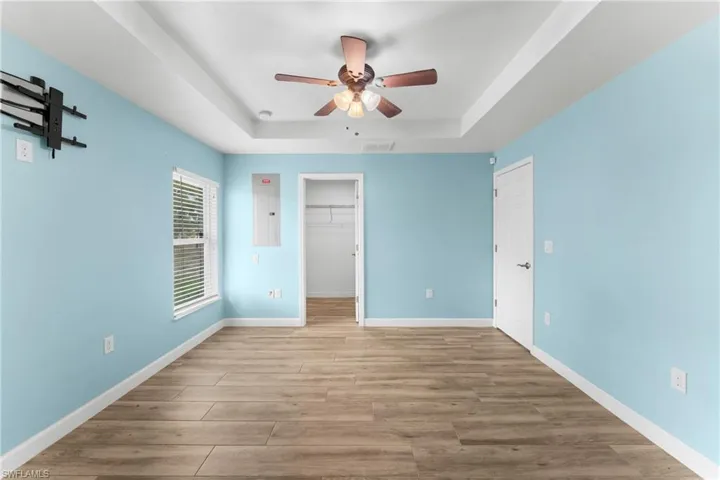 Unfurnished bedroom featuring a spacious closet, light wood-type flooring, electric panel, a ceiling fan, and a raised ceiling