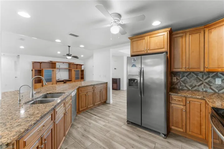 Kitchen featuring stainless steel appliances, light stone counters, a ceiling fan, light wood finished floors, and wood finish cabinets