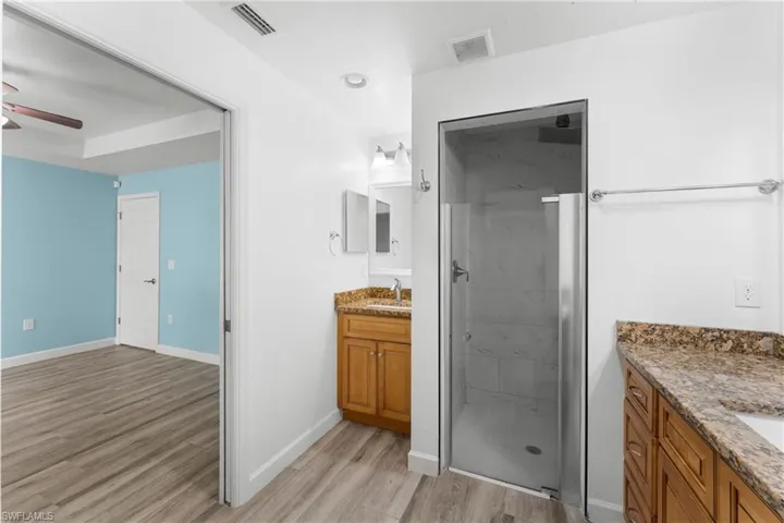 Bathroom featuring two vanities, a ceiling fan, light wood-style floors, and a marble finish shower