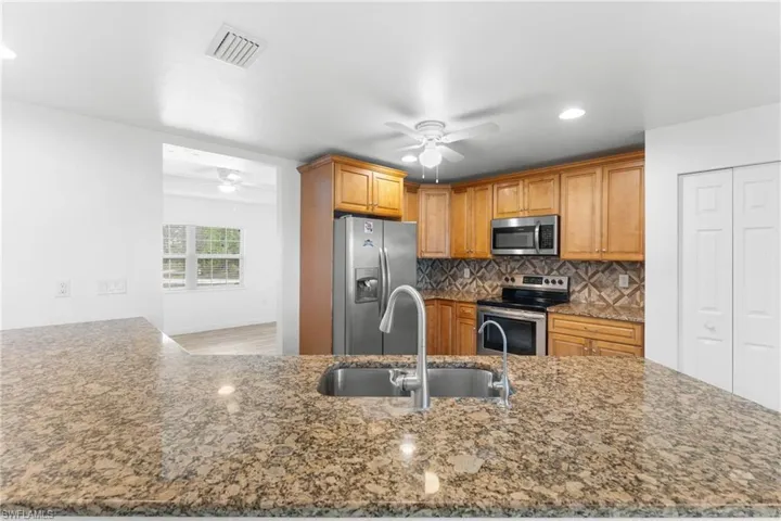 Kitchen with stainless steel appliances, a ceiling fan, dark stone counters, tasteful backsplash, and recessed lighting