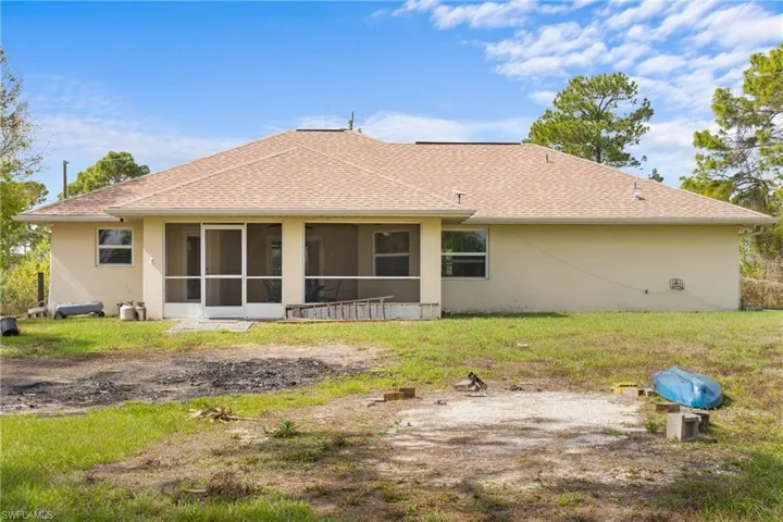 Rear view of house with a sunroom, stucco siding, roof with shingles, and a yard