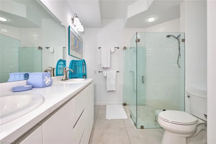 Bathroom featuring toilet, a shower stall, double vanity, and marble finish flooring