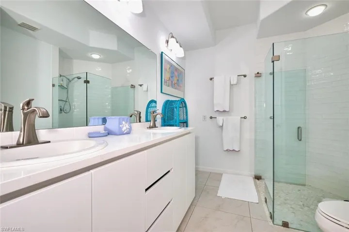 Full bath with a shower stall, double vanity, toilet, and baseboards