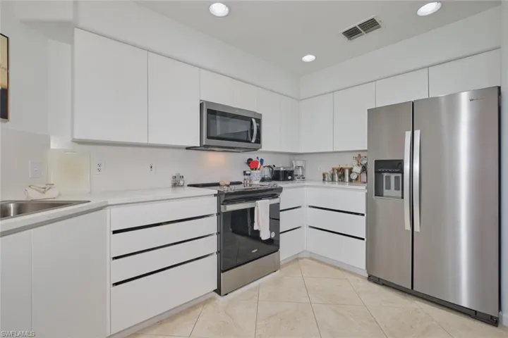 Kitchen with appliances with stainless steel finishes, light countertops, white cabinetry, a sink, and light tile patterned floors