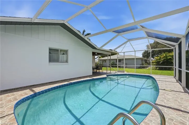 Screen-enclosed freeform pool with blue tile edging and stainless steel handrails, set on a textured paver deck