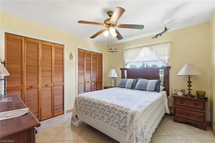 Bedroom featuring tiled flooring, louvered bi-fold closet doors, a ceiling fan with integrated lighting, and a prominent window
