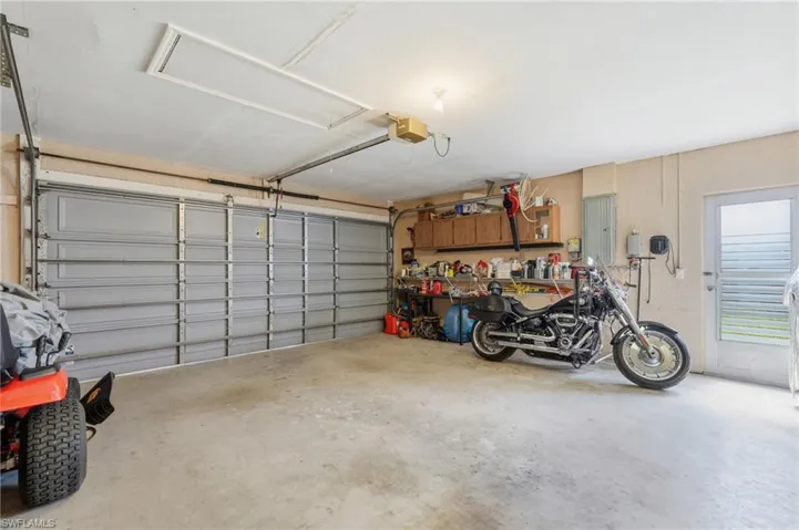 Spacious garage featuring a grey sectional garage door, concrete flooring, overhead lighting, and a side entry door with frosted glass