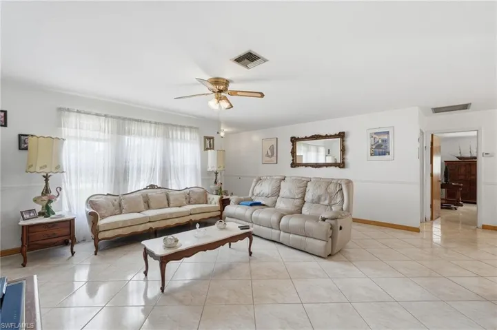 Spacious living area featuring large format tile flooring, a wide window with sheer coverings, and a ceiling fan with integrated lighting
