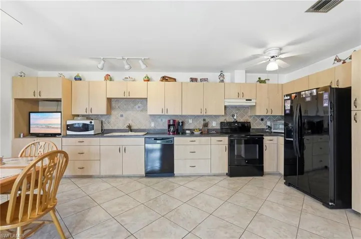 Kitchen featuring light wood-finish cabinetry, black appliances, solid surface countertops, and a tiled backsplash
