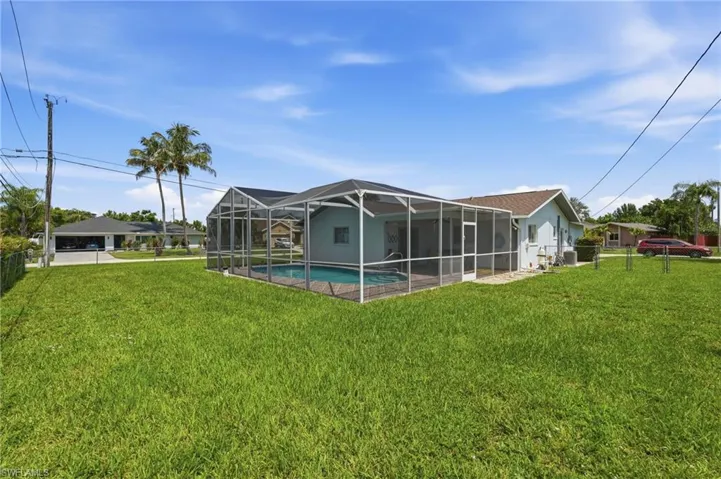 Expansive grassy yard featuring a screened-in swimming pool and a light blue exterior