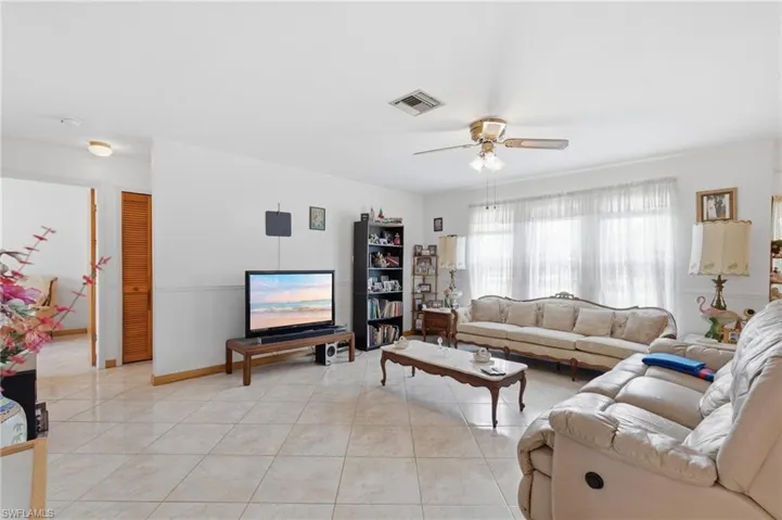 Spacious living area featuring large windows with sheer coverings, ceiling fan with integrated lighting, and tile flooring throughout