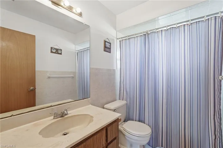 Bathroom featuring a single vanity with an integrated sink, a large wall-mounted mirror, a toilet, and a tiled shower area