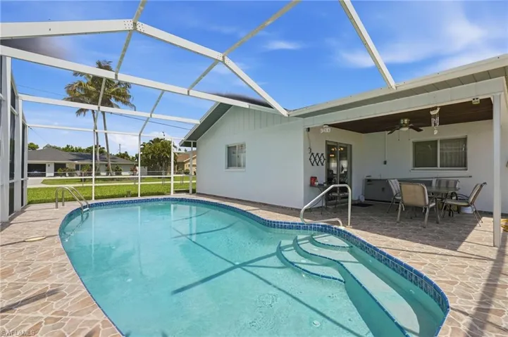 Screened-in swimming pool with integrated steps, surrounded by stone-finish decking
