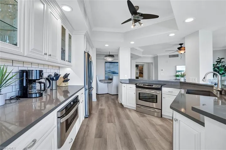 Kitchen with decorative backsplash, light hardwood / wood-style flooring, ceiling fan, appliances with stainless steel finishes, and sink
