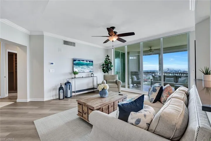 Living room featuring ceiling fan, a wall of windows, ornamental molding, and light hardwood / wood-style floors