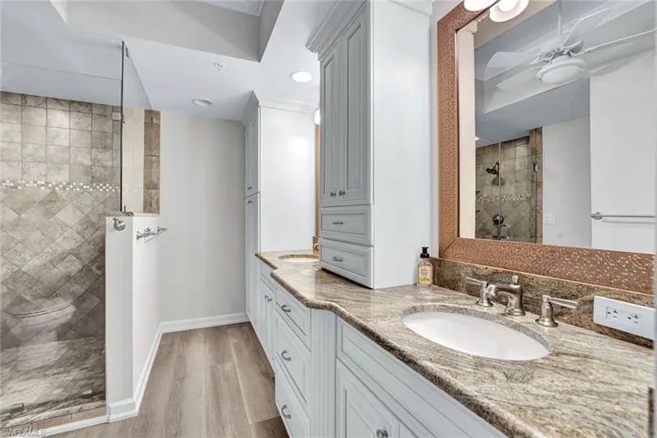 Bathroom with double vanity, a tile shower, hardwood / wood-style floors, and ceiling fan