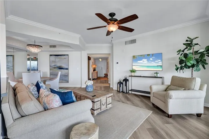 Living room with light hardwood / wood-style flooring, ceiling fan with notable chandelier, and crown molding
