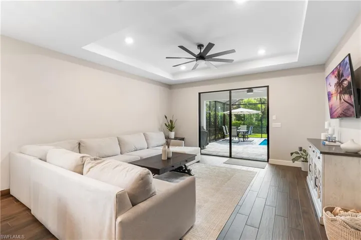 Living room featuring dark wood-type flooring, a ceiling fan, a tray ceiling, and recessed lighting