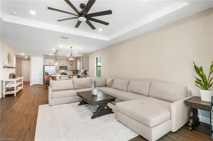 Living area featuring a tray ceiling, dark wood-type flooring, recessed lighting, a chandelier, and a ceiling fan